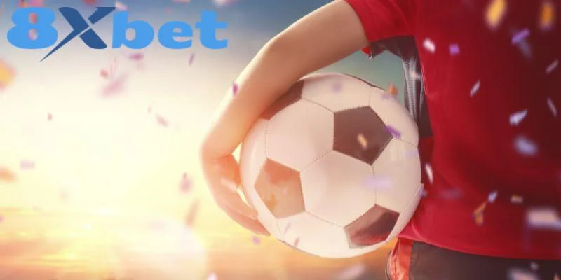 Người mặc áo đỏ kẹp quả bóng bên hông giữa pháo giấy, có logo 8Xbet, minh họa kèo bóng đá AFF Cup