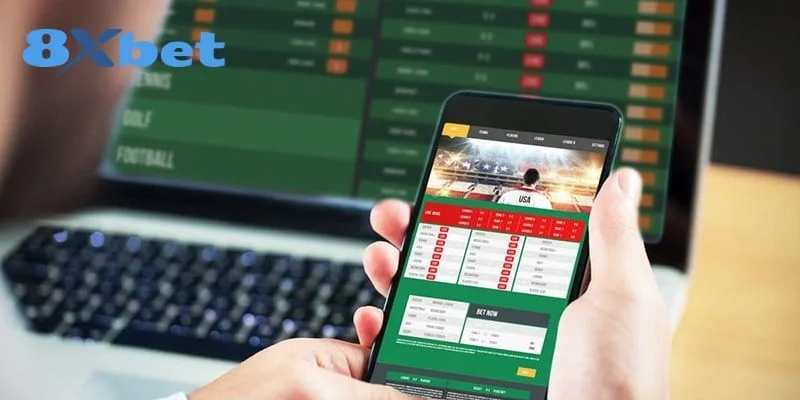 Người dùng cầm điện thoại mở trang cá cược thể thao 8xbet khi gặp lỗi 8xbet không vào được trước màn hình laptop, góc trên có logo 8Xbet.